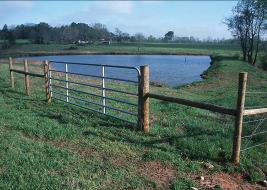 Picture of a pasture with a fence and pond.